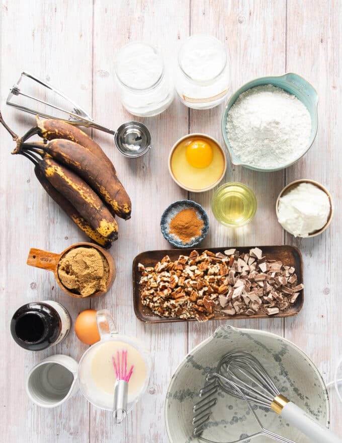 ingredients needed to make banana bread muffins in small bowls including ripe bananas, egg, brown sugar, yogurt, vanilla, a bowl of dry ingredients, a bowl of oil
