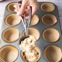 An ice cream scoop filled with muffin batter is scoping the batter into muffin tins