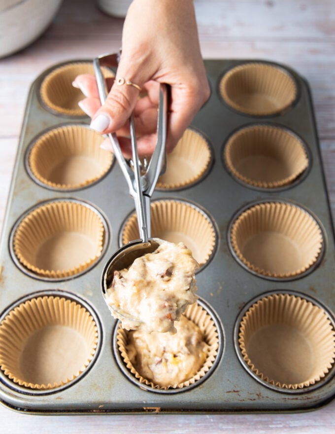 An ice cream scoop filled with muffin batter is scoping the batter into muffin tins