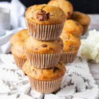 three banana bread muffins stacked up one over the other showing close up the golden tops with chocolate chunks studded and the fluffy tall bakery style muffins