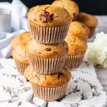 three banana bread muffins stacked up one over the other showing close up the golden tops with chocolate chunks studded and the fluffy tall bakery style muffins