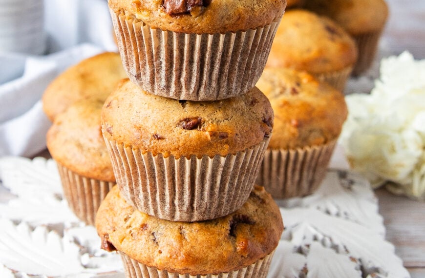 three banana bread muffins stacked up one over the other showing close up the golden tops with chocolate chunks studded and the fluffy tall bakery style muffins