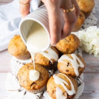A hand drizzling some cream cheese glaze over the banana bread muffins for an extra divine touch to the muffins