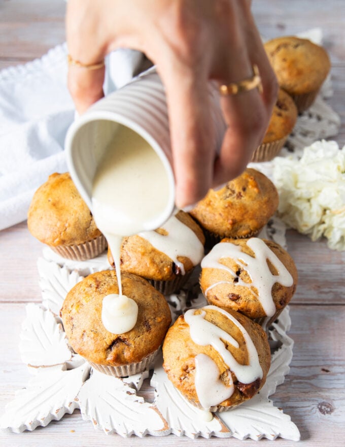 A hand drizzling some cream cheese glaze over the banana bread muffins for an extra divine touch to the muffins