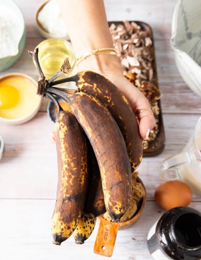 A hand holding a bunch of brown overripe bananas showing how they should look