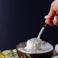 A hand holding a spoon in to the garlic parmesan sauce showing the creamy consistency of the sauce