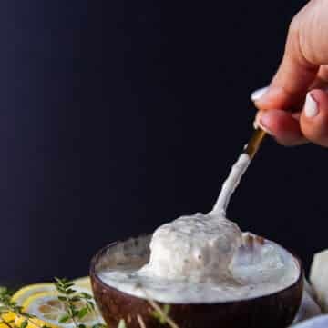 A hand holding a spoon in to the garlic parmesan sauce showing the creamy consistency of the sauce