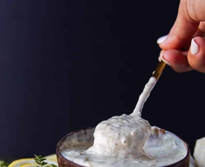 A hand holding a spoon in to the garlic parmesan sauce showing the creamy consistency of the sauce