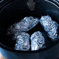 The seasoned hasselback sweet potatoes wrapped individually in foil and placed in an air fryer basket
