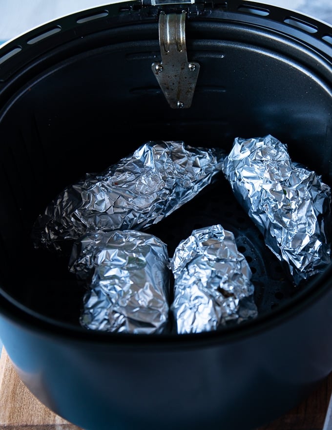 The seasoned hasselback sweet potatoes wrapped individually in foil and placed in an air fryer basket