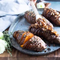 A spoon adding some extra cinnamon sugar pecan butter over the sweet flavored hasselback sweet ptatoes