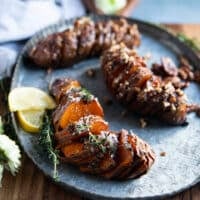 hassleback sweet potatoes on a serving platter showing the thin slices and the layers of herbs or pecans flavoring for a sweet and savory version