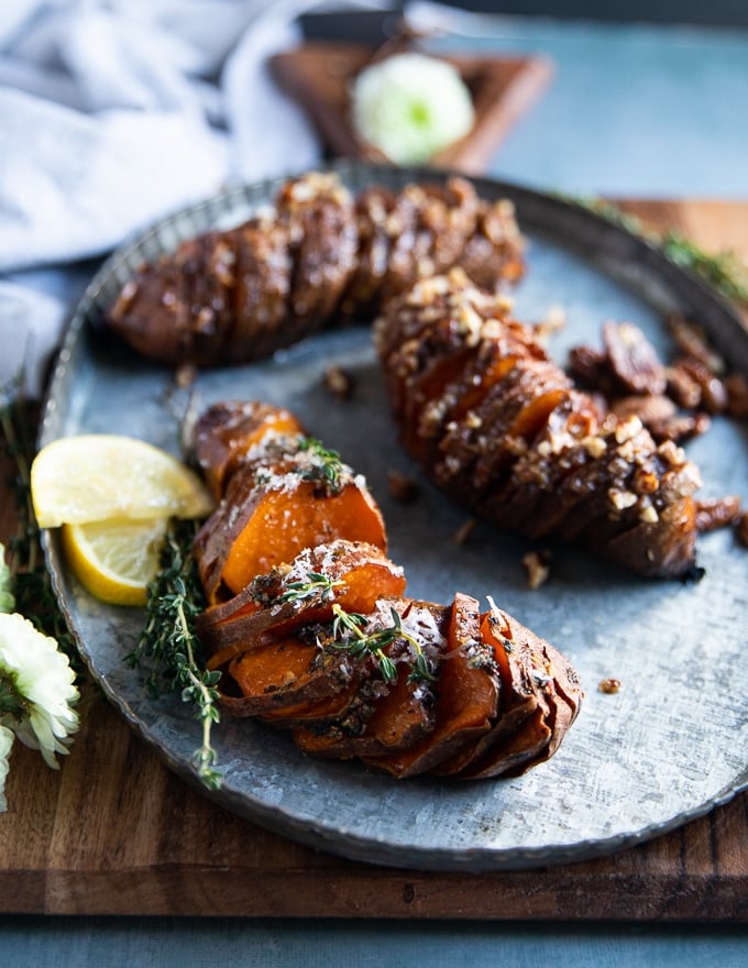 hassleback sweet potatoes on a serving platter showing the thin slices and the layers of herbs or pecans flavoring for a sweet and savory version