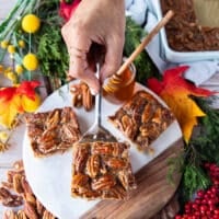 A hand holding a square spatula removing the first square from the pan of the pecan pie bars recipe