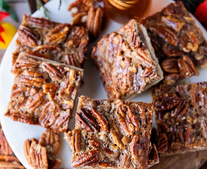Pecan pie bars stacked on a white marble and a top view show close up of one pecan pie bar with the pecans arranged