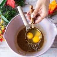 A hand ready to pour the eggs one at a time into the warm caramel mixture while the other hand holding a whisk to whisk continuously