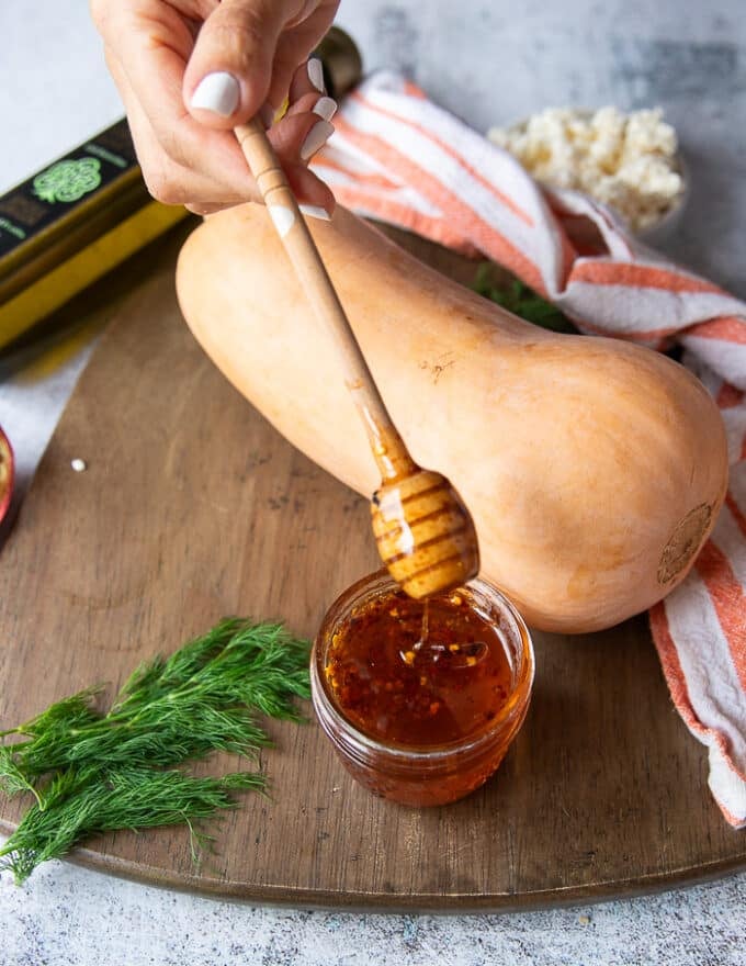 A hand holding a jar of hot honey to drizzle over the butternut squash