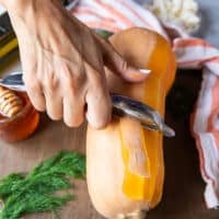 A hand peeling the butternut squash using the peeler