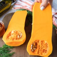 A hand holding a cut up half of butternut squash showing the seeds and texture of the veggie