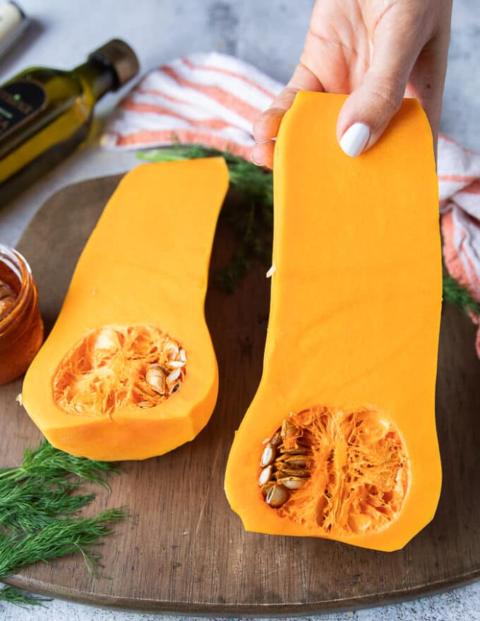 A hand holding a cut up half of butternut squash showing the seeds and texture of the veggie 