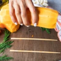 A hand showing how to cut the squash by placing one half on the wooden board