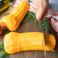 A knife thinly slicing the butternut squash