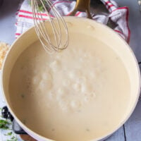 the creamy sauce bubbly and ready with a hand holding a whisk