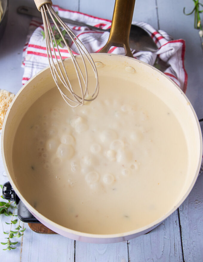 the creamy sauce bubbly and ready with a hand holding a whisk
