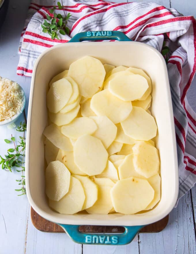 scalloped potatoes layering begins with half of the sliced potatoes at the bottom of a 9 by 13 inch baking dish