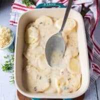 A ladle pouring half of the cream sauce over the potatoes layering to make the scalloped potatoes