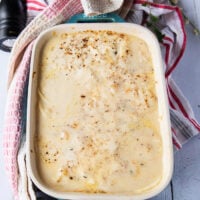 The scalloped potatoes uncovered halfway through baking showing how the potatoes have released some moisture into the sauce and the dish is retuned back to the oven