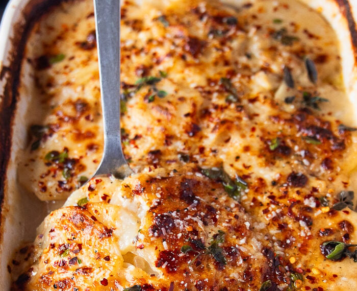 close up of scalloped potatoes portion removed with a spoon showing the texture of the cooked soft potatoes and a cheesy top golden crust