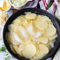 Thinly sliced potatoes in a bowl of ice cold water