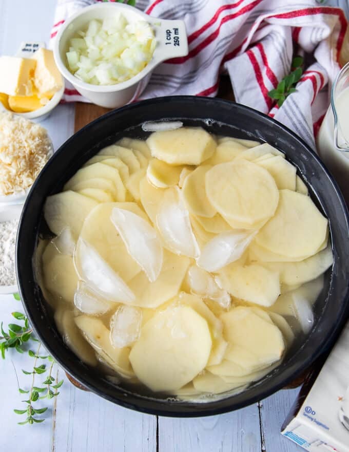 Thinly sliced potatoes in a bowl of ice cold water