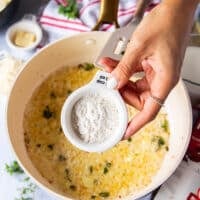 A hand holding the flour to be added to the sauce once the onions are ready