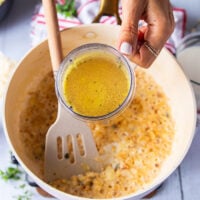 A hand pouring the stock in to the onions and flour mixture to start making the sauce