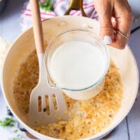 A hand pouring in the milk into the pan