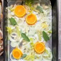 A roasting pan ready and layered with onion rings, orange slices, celery and sage at the bottom