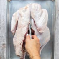 A hand holding a scissors and starting to cut through one side of the back bone of the turkey