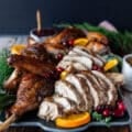 carved spatchcock turkey on a serving plate with orange slices, cranberry sauce and fresh cranberries