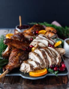 carved spatchcock turkey on a serving plate with orange slices, cranberry sauce and fresh cranberries