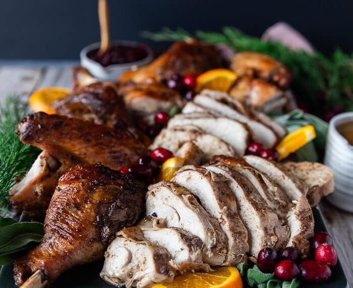 carved spatchcock turkey on a serving plate with orange slices, cranberry sauce and fresh cranberries