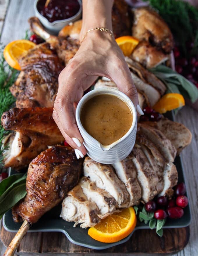A hand holding a gravy boat made using the pan dripping of the turkey and ready to pour over the craved and sliced spatchcock turkey recipe on the platter