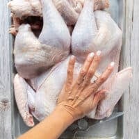 A hand pressing firmly on the breast bone of the turkey to crack it and flatten the turkey