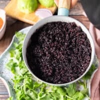 The cooked wild rice in a pan being added over the plate of arugula