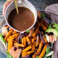 A hand drizzling the cranberry sauce over the sweet potato salad