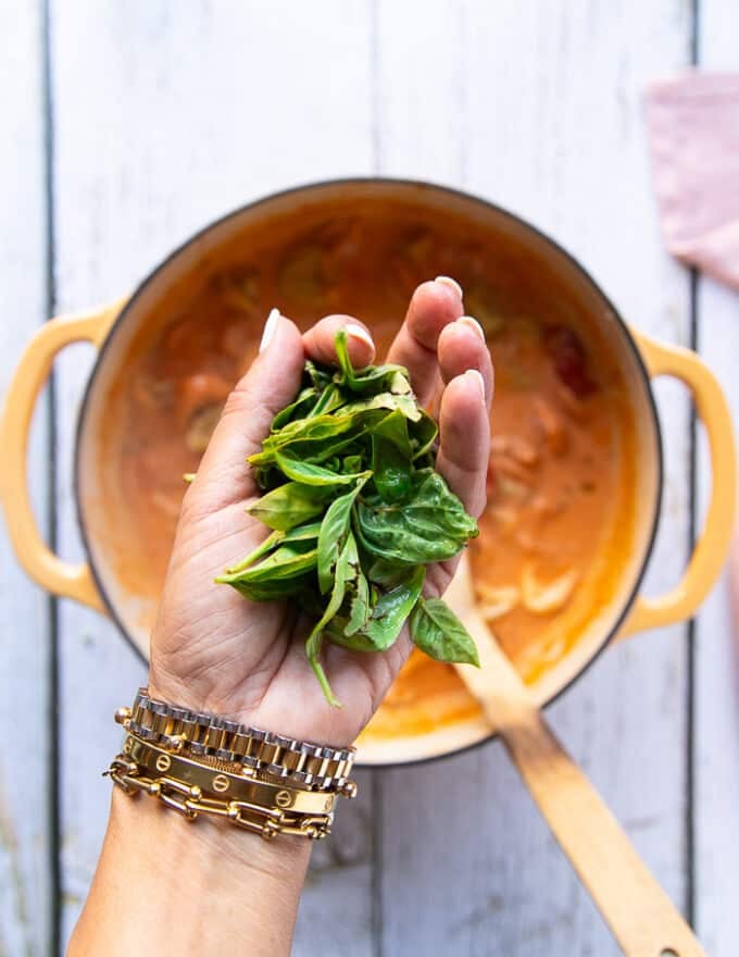 A hand holding fresh basil leaves whole and adding it to the tortellini soup as a final step to complete the recipe