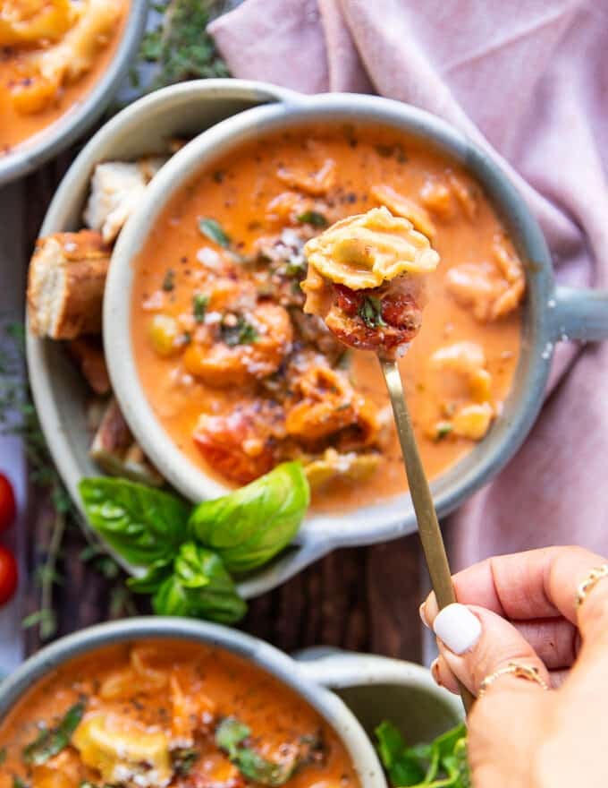 A spoon scooping out on tortellini in the soup showing the cooked tortellini and the saucy soup broth