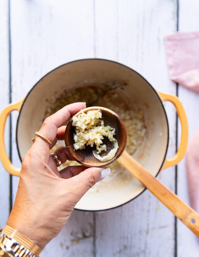 A hand holding the minced garlic in a bowl ready to add to the soup