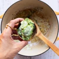A hand holding the basil pesto in a bowl ready to add to the soup